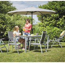 Gartenszene mit Esstisch, Stühlen, Liegestuhl und Sonnenschirm auf einer Rasenfläche