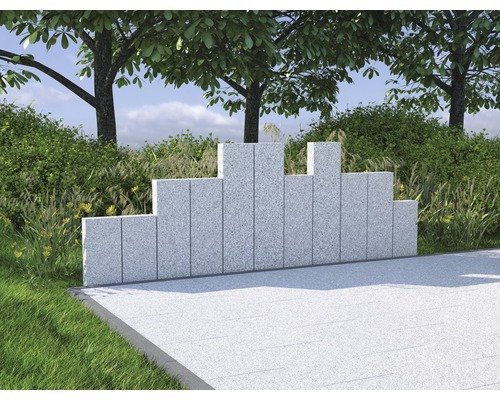 Dekorative Gartenmauer aus Granit vor Büschen und Bäumen