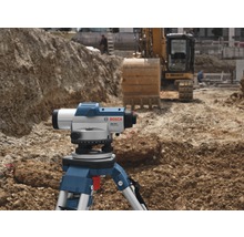 Baustellenszene mit Nivelliergerät auf Stativ und Bagger im Hintergrund