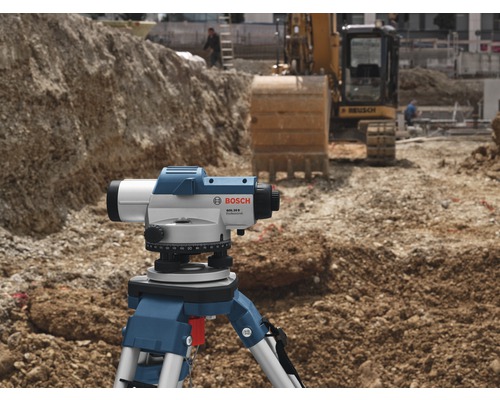 Baustellenszene mit Nivelliergerät auf Stativ und Bagger im Hintergrund