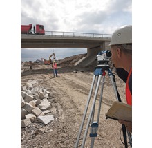 Bauarbeiter vermessen Baustelle mit Nivelliergerät unter Brücke.