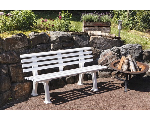 Gartenszene mit einer weißen Gartenbank aus Holz und einer Feuerstelle aus Metall.