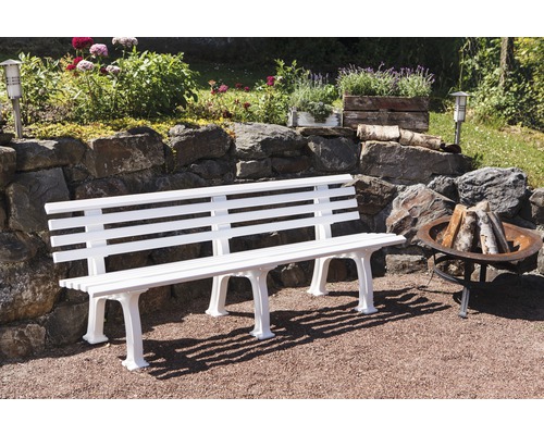 Gartenlandschaft mit einer weißen Gartenbank aus Kunststoff, einem Steingarten und einer Feuerstelle.