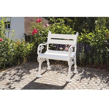 Weiße Gartenbank aus Metall auf einem gepflasterten Bereich vor Büschen und Blumen