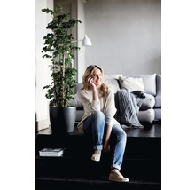 Helle, freundliche Wohnzene mit einer Frau, die auf einer Treppe sitzt, einer Zimmerpflanze im Topf und einem Sofa