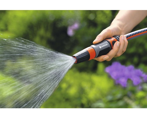 Eine Person hält einen Gartenschlauch mit Spritzdüse in der Hand, aus der Wasser austritt.