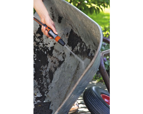 Eine Person reinigt eine schmutzige Schubkarre mit einer Gartenspritze.