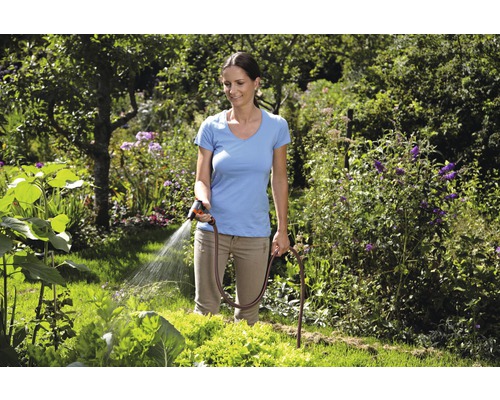Frau bewässert Garten mit Gartenschlauch und Spritzpistole
