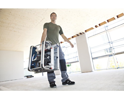 Ein Mann trägt eine Tischkreissäge in einem Raum im Bau.