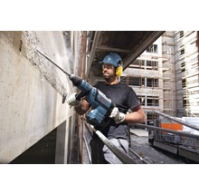 Ein Bauarbeiter mit Schutzhelm und Gehörschutz arbeitet mit einem Abbruchhammer an einer Betonwand. Bosch Logo.