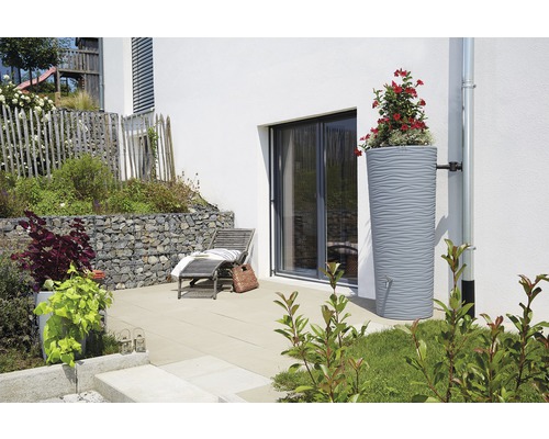 Regenspeicher mit Bepflanzung neben einem Haus mit Terrasse und Liegestuhl