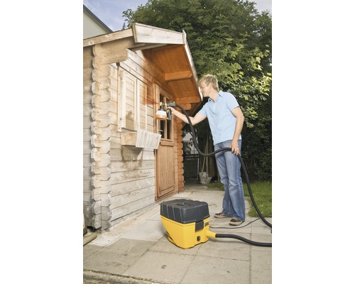 Mann sprüht Farbe auf ein Holzhaus mit einem Farbsprühsystem.