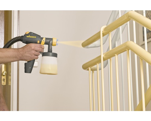 Eine Person lackiert mit einem Farbsprühsystem ein Treppengeländer.