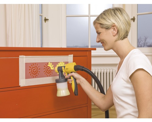 Frau verwendet Farbsprühgerät auf Kommode mit Sonnenschablonen