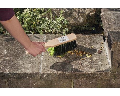 Hand fegt mit einer Kehrbürste eine Steintreppe