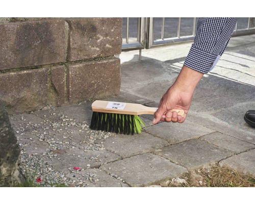 Eine Person benutzt eine Kehrbürste mit Holzgriff zur Reinigung von Pflastersteinen.