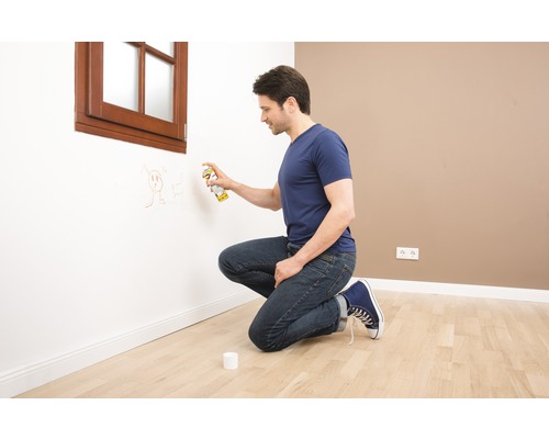 Mann entfernt Zeichnungen mit Lackspray von einer Wand in einem Raum.