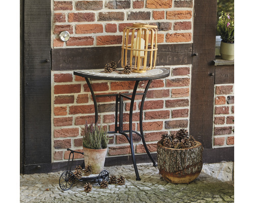 Dekorative Szene mit Tisch, Laterne, Pflanzen und Tannenzapfen vor einer Backsteinmauer