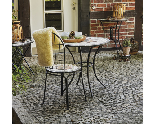 Gartenszene mit Mosaiktisch, Stuhl mit Fellauflage und Beistelltisch auf gepflastertem Untergrund