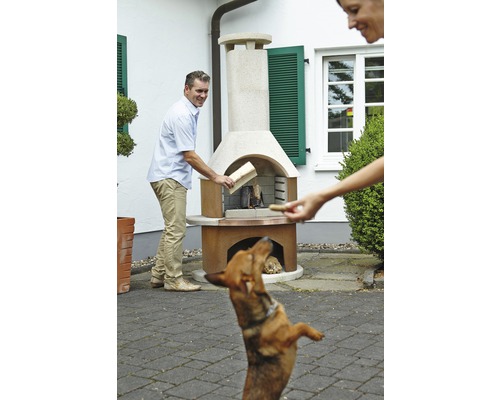 Szene mit einem Mann, der Holz in einen Gartengrill legt, während eine Frau einem Hund ein Leckerli gibt.