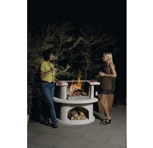 Zwei Frauen stehen an einem Steingrill mit Holz und Feuer.
