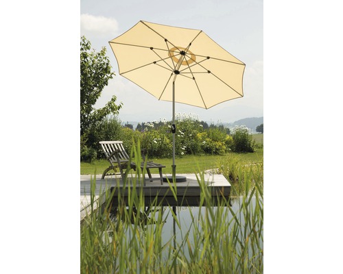 Geöffneter Gartenschirm neben einem Liegestuhl auf einer Terrasse am Gartenteich