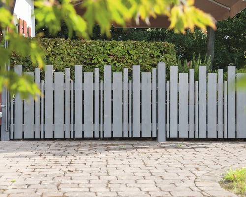 Grauer Holzzaun mit vertikalen Brettern unterschiedlicher Höhe