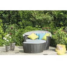 Gartenmöbel-Set mit Rattan-Optik und farbigen Kissen vor grüner Hecke