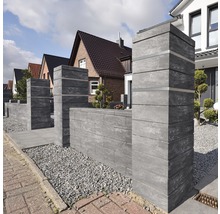 Außenaufnahme einer Gartenzaunmauer aus Betonsteinen vor Wohnhäusern.
