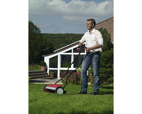 Ein Mann benutzt einen Rasenkehrer auf einem Rasen vor einem Haus.