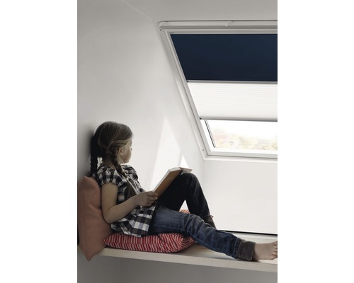 Mädchen sitzt am Dachfenster mit Verdunkelungsrollo und Wabenplissee und liest ein Buch
