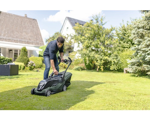 Mann bedient einen Akku-Rasenmäher im Garten.