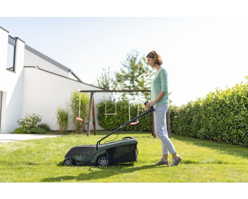 Frau mäht Rasen mit einem Rasenmäher im Garten.
