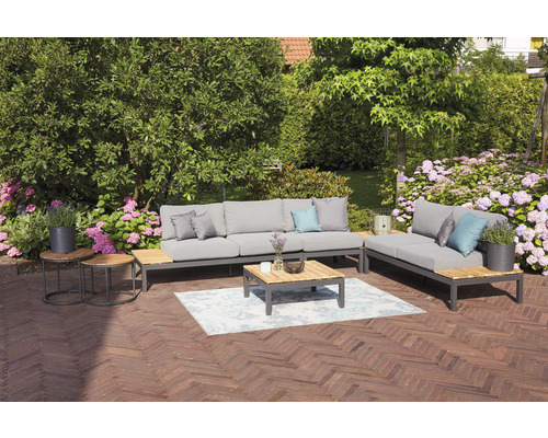 Gartensitzgruppe mit Sofa, Liege, Couchtisch und Beistelltischen auf einer Terrasse mit Blumen im Hintergrund.