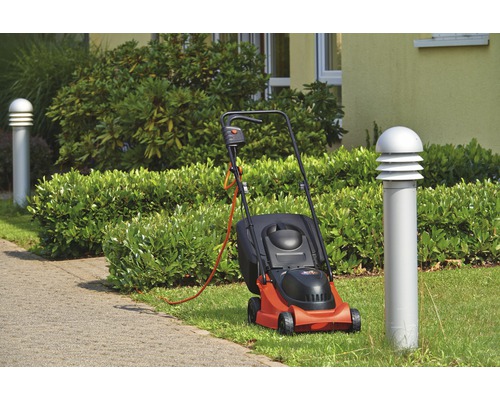 Elektrorasenmäher auf Rasenfläche neben einem Gehweg