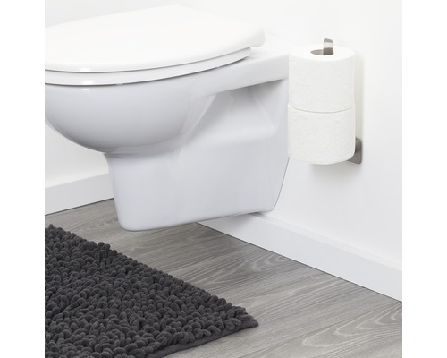 Hänge-WC, Toilettenpapierhalter und Badteppich in einem Badezimmer