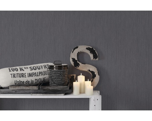 Dekorative Elemente wie Kissen, Behälter, Kerzen und ein großes S auf einem weißen Regal vor einer grauen Wand