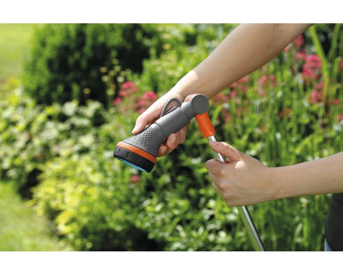 Gartenschlauch mit Sprühkopf in der Hand vor Grünpflanzen