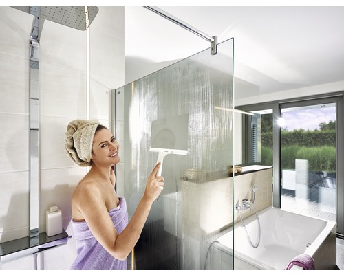 Helle Badezimmerszene mit Duschabtrennung, Brausekopf, Badewanne und Frau, die eine Duschwand mit einem Abzieher reinigt