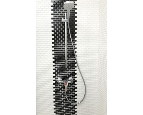 Duscharmatur mit Handbrause vor Wand mit schwarzen und weißen Fliesen