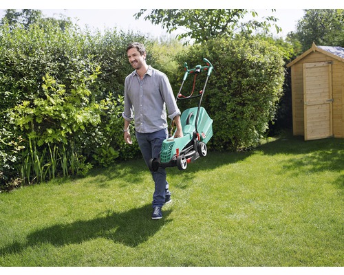 Ein Mann trägt einen Rasenmäher durch einen grünen Garten.