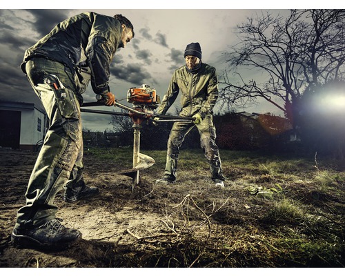 Zwei Arbeiter bohren mit einer Erdlochbohrmaschine ein Loch in den Boden.