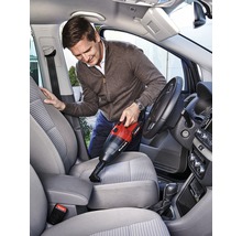 Mann saugt mit einem Akku-Handsauger den Innenraum eines Autos. Der Staubsauger ist rot und schwarz.