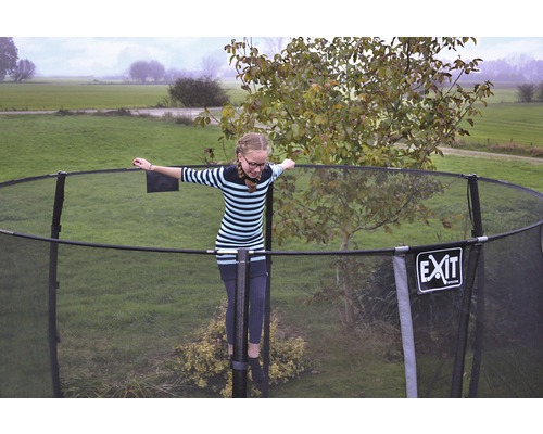 Mädchen balanciert auf einem Gartentrampolin mit Sicherheitsnetz. EXIT Logo.