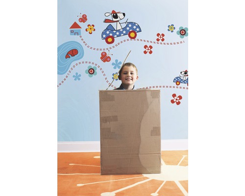 Junge in einem Karton vor einer Wand mit Wandtattoos.