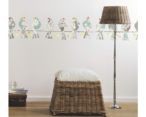 Raumansicht mit Vogelbordüre, Korbhocker, Kissen und Stehlampe.