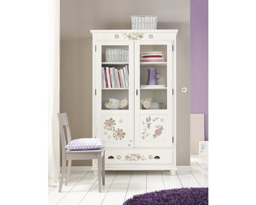 Dekorativer Vitrinenschrank mit floralen Elementen in einem hellen Raum.