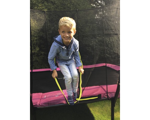 Ein Kind klettert auf ein Gartentrampolin mit Sicherheitsnetz.