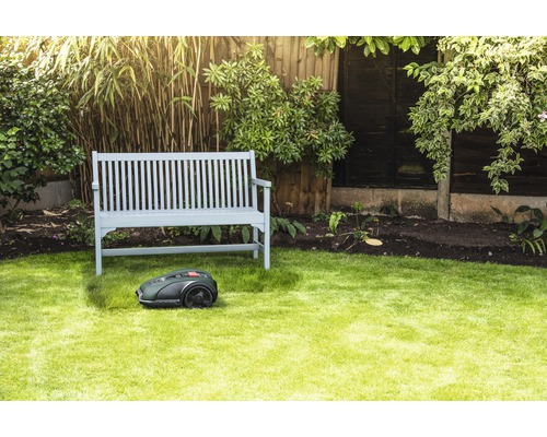 Szene mit einem Rasenmähroboter vor einer Holzbank in einem Garten.