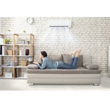 Frau liegt auf Sofa unter Klimaanlage mit Laptop